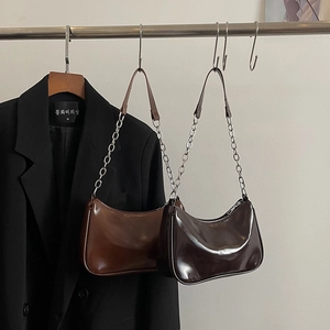 Close-up of caramel and dark brown glossy leather underarm bags with silver chain detail