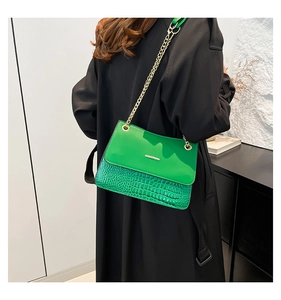 Detail of green faux crocodile leather bag with gold chain strap on a model