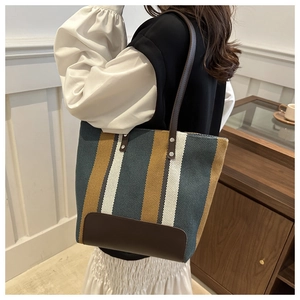 Detail of striped canvas tote bag featuring brown leather straps and reinforced corners