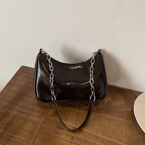 Detail of glossy dark brown hobo bag with thick silver chain on a wooden table