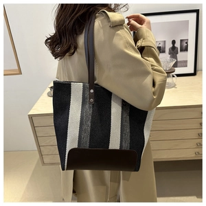 Detailed back view of a striped canvas tote bag with leather straps on a model