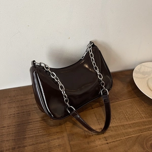 Detail of glossy chocolate brown crescent underarm bag with silver chain on wood surface