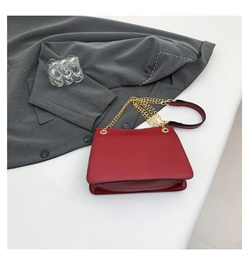 Detail of red matte leather handbag with elegant gold metal chain strap on grey fabric