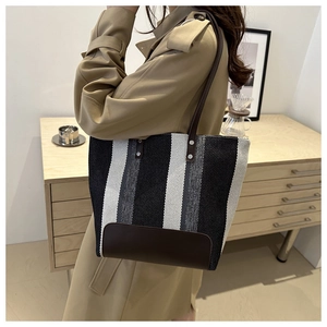 Detail view of a large striped canvas tote bag with leather straps and rivet accents
