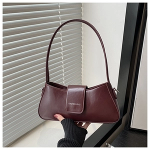 Detail of burgundy underarm bag with silver logo in minimalist indoor sunlight