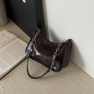 Detailed side view of a glossy dark chocolate crescent bag with silver chain on a table