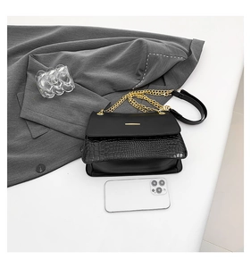 Detail of vintage black chain bag with crocodile texture next to a smartphone