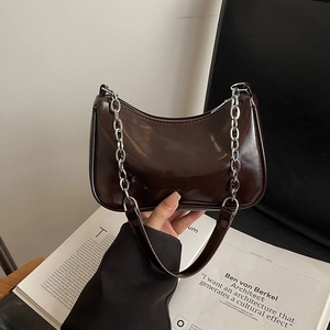 Close-up of a dark brown crescent bag with silver chain detail on a magazine