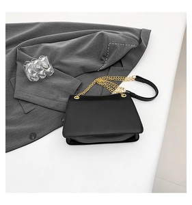 Detail of black trapezoid shoulder bag with elegant gold multi-strand chain strap and pad