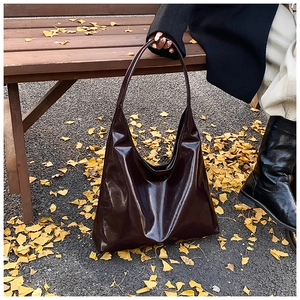 Detail of glossy deep brown hobo tote bag on autumn leaves with a sleek mirror finish