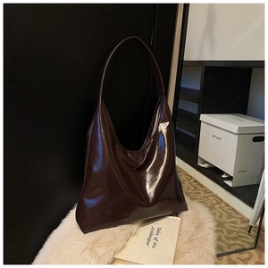 Detail of glossy dark brown leather hobo tote bag on white plush surface in studio