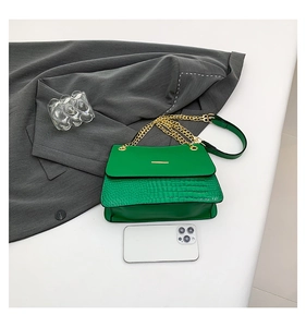 Detail of green crocodile textured handbag with gold chain strap on grey fabric