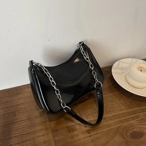 Detail of black glossy crescent bag with silver chunky chain on a dark wooden table