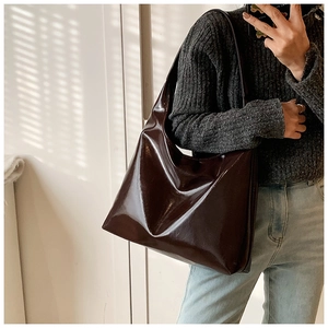 Detail view of large dark brown patent leather tote bag over shoulder in soft light