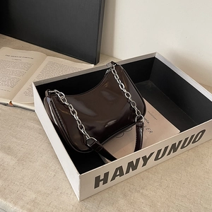 Detail of dark brown glossy patent leather half-moon bag with silver metal chain
