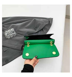 Detailed view of green leather bag featuring golden magnetic snap and chain hook