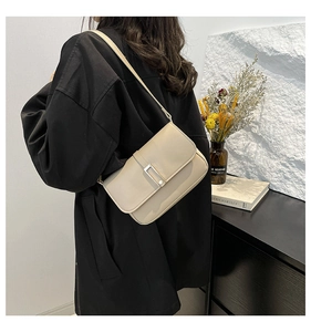 Dettaglio di una borsa a tracolla in pelle beige con fibbia metallica indossata da una modella