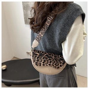 Detail of leopard print strap and beige saddle bag worn by a model in minimalist setting
