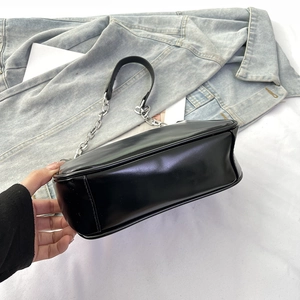 Close-up of black glossy shoulder bag with silver metal chain strap on denim background