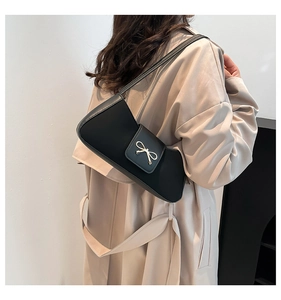Schwarze Schultertasche mit silberner Schleife getragen zu einem beigen Trenchcoat