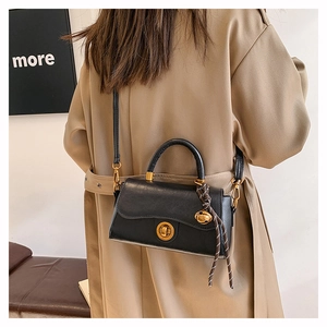 Detail of black leather handbag with golden twist lock and decorative woven pendant knot