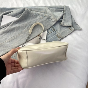 Close-up of cream leather shoulder bag with silver chain strap on white bedding