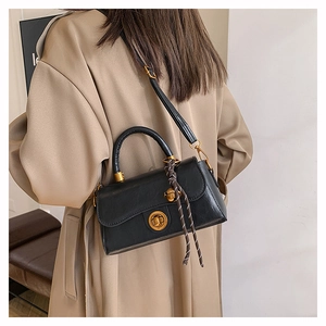 Detail view of a black vintage crossbody bag with gold lock on a khaki trench coat