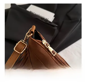 Close-up of brown suede tassel bag with glossy gold zipper and adjustable strap