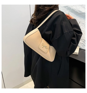 Detail einer cremefarbenen Kunstleder-Schultertasche mit goldener Schleife als Magnetverschluss
