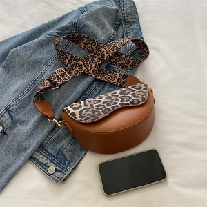 Brown faux leather saddle bag with leopard print flap and wide strap on denim backdrop