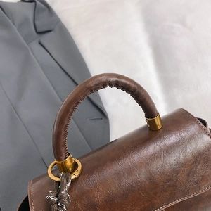 Retro brown leather handbag for women featuring gold hardware and a woven charm detail