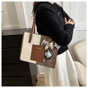 Detail of color-block tote bag with FASHION logo and elegant silk scarf on handle
