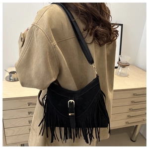 Detail of a black suede crossbody bag featuring long tassels and a gold metal buckle