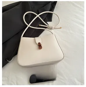 Detail of a creamy white crescent bag with a decorative knot strap and vintage buckle