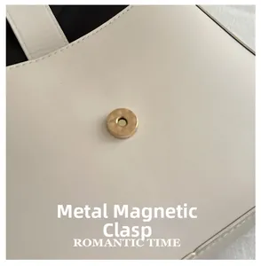 Close-up of golden magnetic buckle on white leather baguette bag with stitching