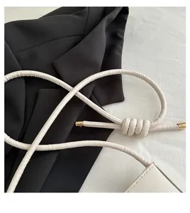 Detail view of cream white crescent bag featuring cylindrical knotted handle and gold metal caps