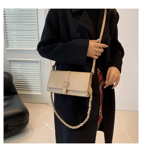 Détail d'un sac bandoulière beige avec boucle décorative et bandoulière en chaîne tressée
