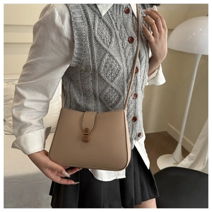 Detail of a chic cream leather crescent shoulder bag with metal buckle on a model