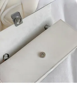 Detail view of the silver magnetic buckle on a white leather handbag with neat stitching