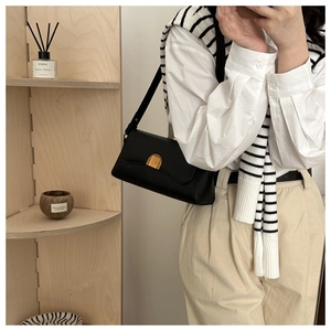 Detail of minimalist black matte leather shoulder bag with a gold crescent buckle closure