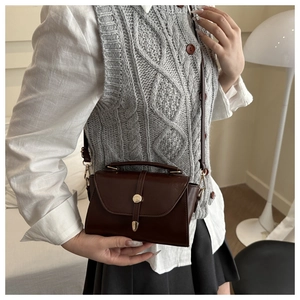 Detail of dark brown vintage handbag featuring a gold cylindrical twist lock and top handle