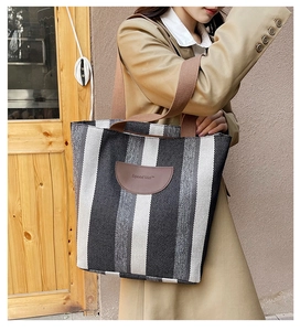 Detail of striped canvas tote bag with brown shoulder straps and leather brand patch