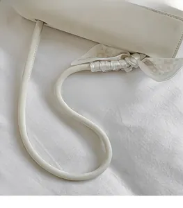 Detail of white faux leather shoulder strap with a plaid silk scarf decorative tie
