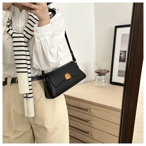 Detail of a minimalist black leather shoulder bag with a square golden metal clasp lock