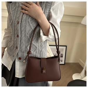 Detail view of brown leather crescent bag with retro metal buckle and knot strap on shoulder