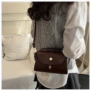 Model shot of a vintage dark brown leather handbag with metal clasp and adjustable strap