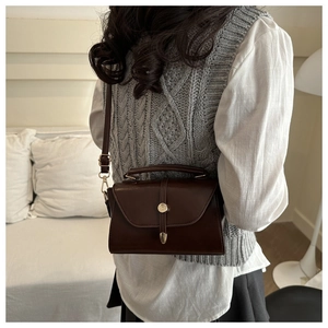 Detail of vintage dark brown leather crossbody bag with gold hardware and top handle