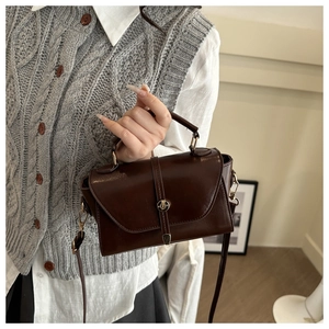 Detail of a deep brown shiny faux leather handbag with a round metal clasp and short handle