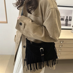 Chic black suede shoulder bag with tassel details and vintage metal buckles in indoor setting