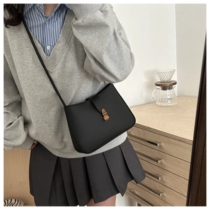 Detail of a matte black crescent shoulder bag with a vintage bronze metal buckle and strap